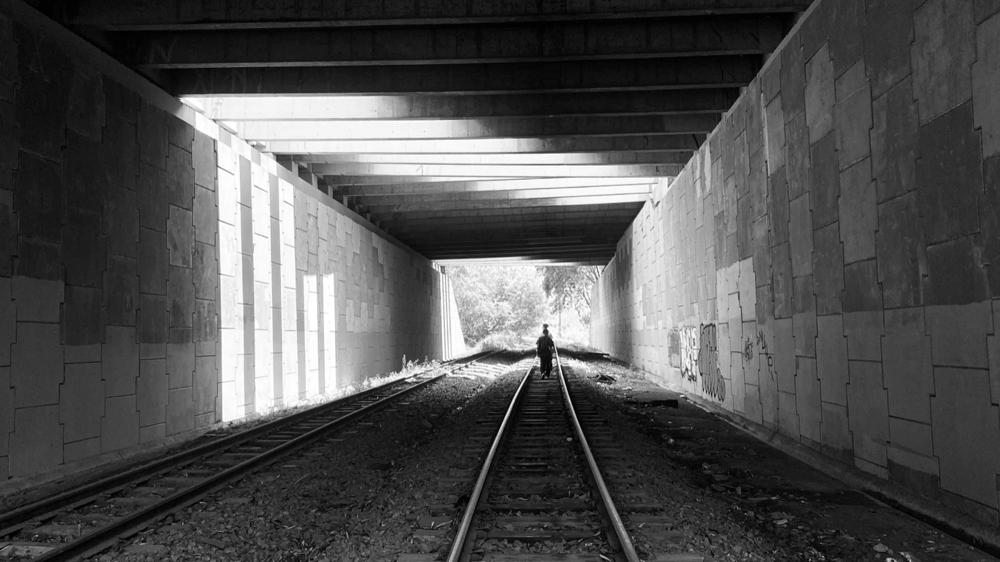 Linha de trem sob viaduto pichado, à noite